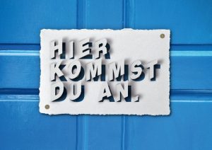 Eine blaue Holztür mit einem Schild "Hier kommst du an."