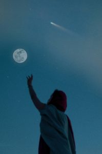 Silhouette einer Person im Vordergrund, deutet auf Vollmond am sternenklaren Himmel; eine Sternschnuppe fliegt vorbei