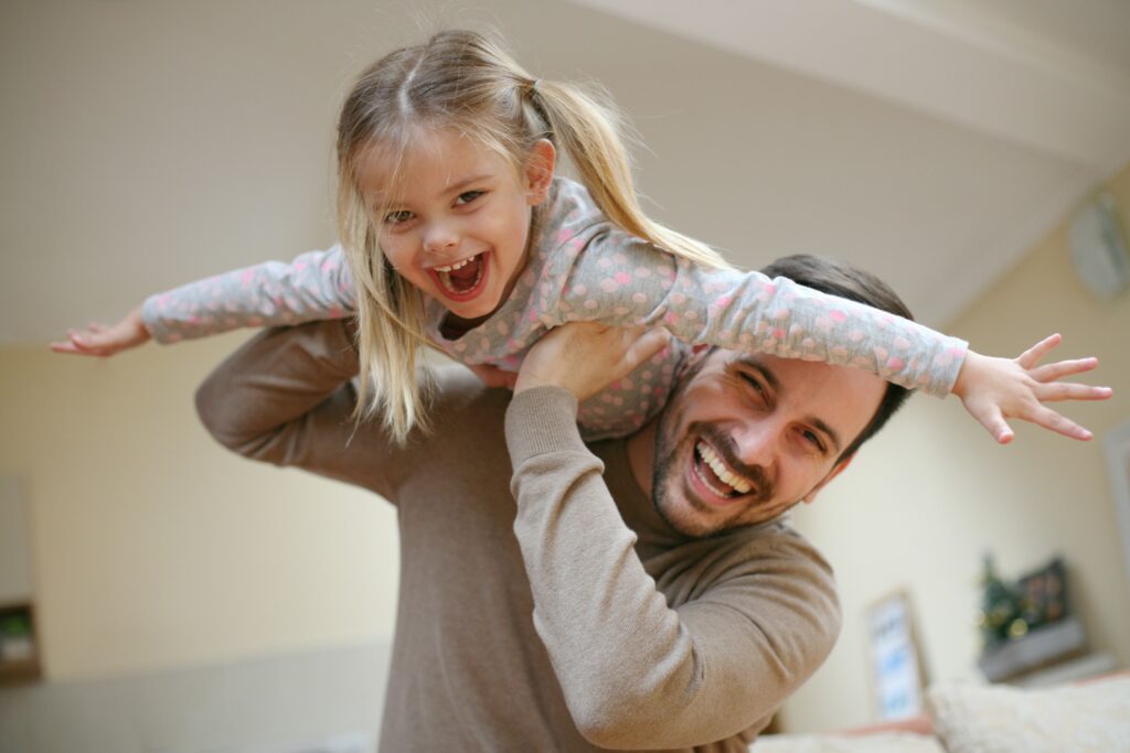 Vater lässt Tochter auf seiner Schulter fliegen: beide lachen