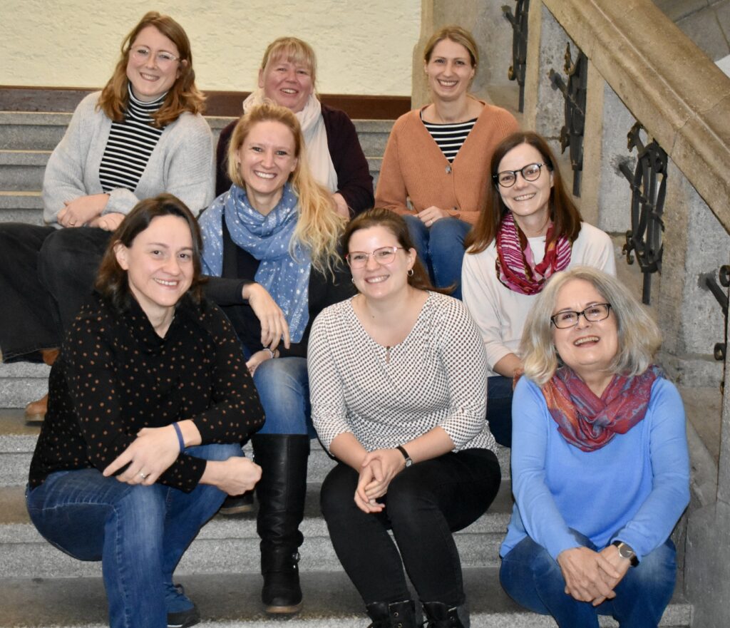 Das Team Familienbildung im EBW Regensburg sitzt auf Stufen und lächelt in die Kamera