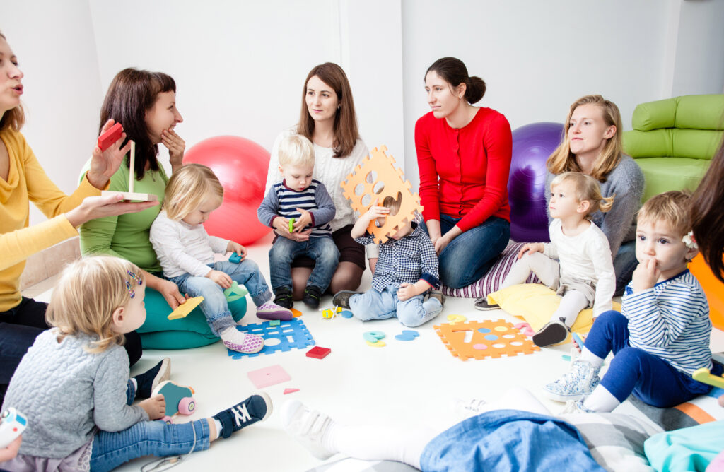 Gruppe von Müttern mit ihren Kindern sitzt am Boden im Kreis in Spielsituation